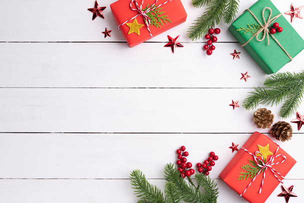 Concepto de fondo de Navidad. Vista superior de la caja de regalo verde y rojo de Navidad con ramas de abeto, conos de pino, bayas rojas y campana sobre fondo de madera blanca
. - Foto, imagen
