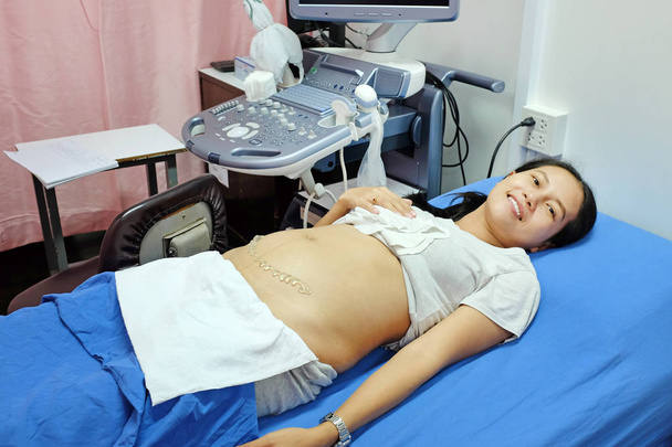 Happy Asian pregnant woman waiting for doctor to ultrasound scanning procedure at the hospital. - Photo, Image