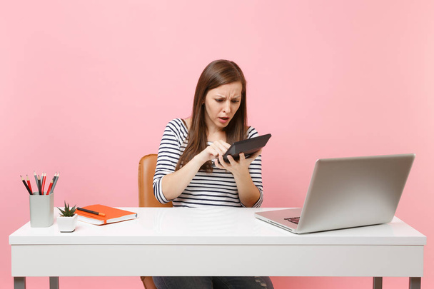 Fiatal nő gazdaság számológéppel aggódik bajok számítások munka irodai pc laptop elszigetelt pasztell rózsaszín háttér ideges. Eredmény üzleti karrier fogalma. Másolja a hely - Fotó, kép