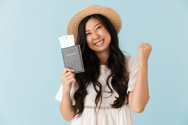 Image of young excited asian beautiful woman isolated over blue background holding passport with tickets. - Valokuva, kuva