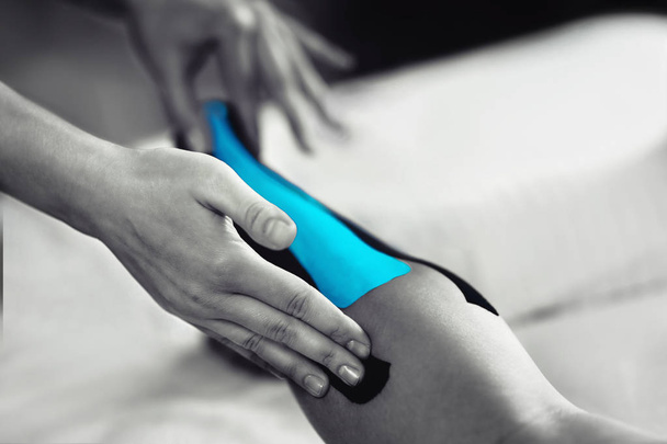 Zwart-wit beeld van kinesiologie tape behandeling met blauwe tape op vrouwelijke patiënt gewond achillespees. Sport letsel kinesio behandeling. - Foto, afbeelding