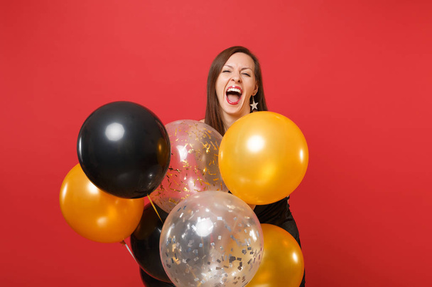Szczęśliwa młoda dziewczyna w czarne ubrania krzyczy świętować przytrzymaj balonów na białym tle na czerwonym tle. Święty Walenty, International Women's dzień szczęśliwy nowy rok urodziny makieta holiday party koncepcja - Zdjęcie, obraz