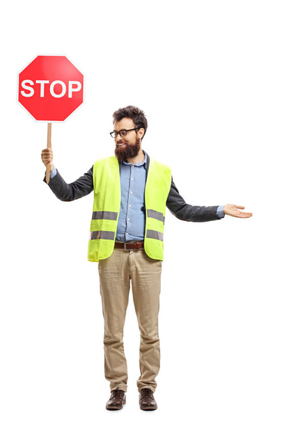 Täyspitkä muotokuva miehestä, jolla on turvaliivi ja stop-merkki, joka osoittaa kädellään ja katsoo toiselle puolelle valkoisella pohjalla eristettynä
 - Valokuva, kuva