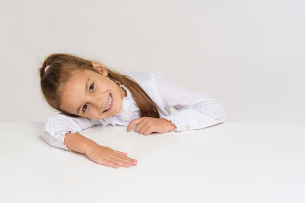 Portrait of a cute baby girl on a white background at the table. The child is right in front of the camera, smiling and looking happy - Fotografie, Obrázek