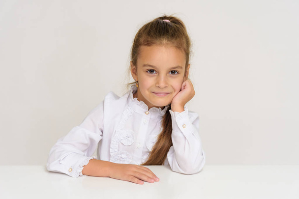 Portrait of a cute baby girl on a white background at the table. The child is right in front of the camera, smiling and looking happy - Fotó, kép