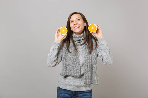 Dreamful young woman in gray sweater, scarf looking up, holding oranges isolated on grey wall background. Healthy fashion lifestyle, people sincere emotions, cold season concept. Mock up copy space - Photo, Image