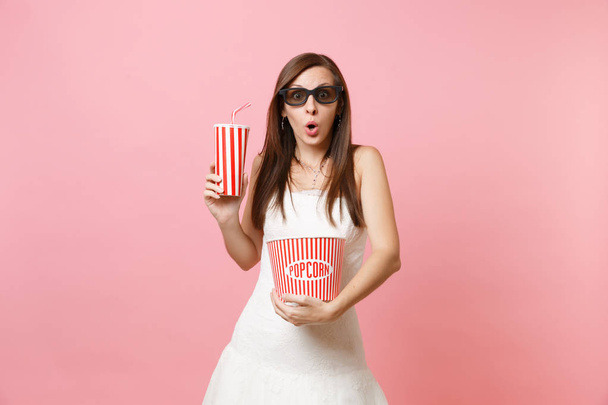 Amazed bride woman in wedding dress, 3d glasses watching movie film, holding bucket of popcorn, plastic cup of soda or cola isolated on pink pastel background. Wedding celebration. Emotions in cinema - Photo, Image