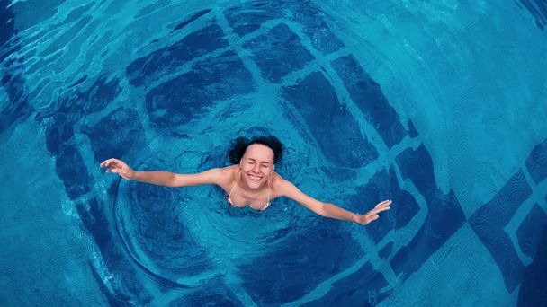 Directly above happy female swimming in a pool. Aerial view - Foto, Imagen