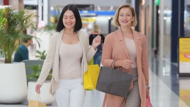 Slow-motion. Twee mooie vrouwen winkelen, wandelen in winkelcentrum en winkelpuien te kijken. Meisjes lachen binnenshuis met grote winkel. - Video