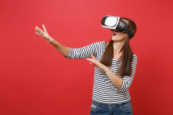 Young girl in virtual reality glasses touch something like push on button pointing at floating virtual screen isolated on red background. People sincere emotions lifestyle concept. Mock up copy space - Photo, Image