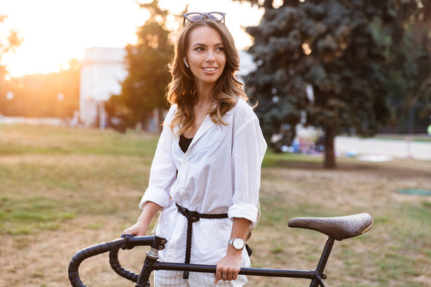 Χαμογελώντας νεαρή γυναίκα ελεύθερος χρόνος στο πάρκο, το περπάτημα με ποδήλατο - Φωτογραφία, εικόνα