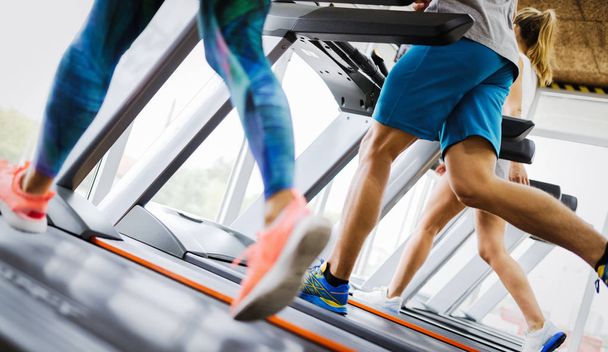 Healthy man and woman running on a treadmill in a gym. Sport and health concept - Photo, image