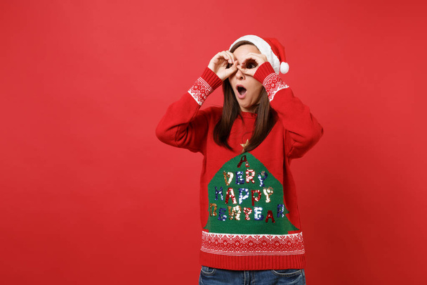 Překvapený Santa girl drží ústa otevřená, držení rukou očima, imitující brýle nebo dalekohled izolovaných na červeném pozadí. Šťastný nový rok 2019 oslavu dovolenou stranou koncept. Vysmívat se kopie prostor - Fotografie, Obrázek
