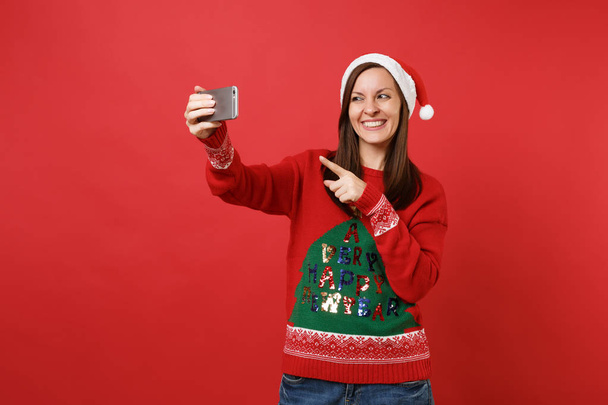 İşaret parmağı parlak kırmızı zemin üzerine izole alarak selfie üstünde hareket eden telefon, atış yapıyor gülümseyen genç Noel Baba kız. Mutlu yeni yıl 2019 kutlama tatil parti kavramı. Kopyalama alanı alay - Fotoğraf, Görsel