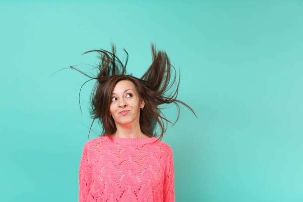 Συλλογισμένος νεαρή γυναίκα στο πλεκτό ροζ πουλόβερ με φτερουγίσματα μαλλιά κοιτώντας ψηλά απομονωθεί σε φόντο μπλε τυρκουάζ τοίχο, στούντιο πορτρέτου. Άνθρωποι ειλικρινή συναισθήματα, αντίληψη του τρόπου ζωής. Κοροϊδεύετε αντίγραφο χώρου - Φωτογραφία, εικόνα