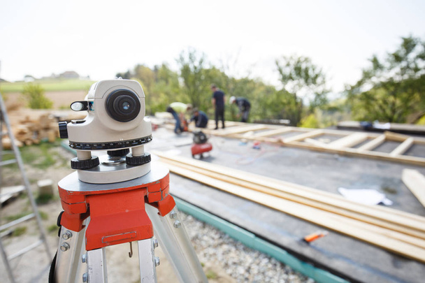 Theodolite measuring angles and positions of modules of prefabricated house. Building industry, carpentry concept with workers in the background erecting the frame. - Photo, image