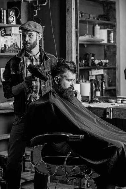 Barber with hairdryer works on hairstyle for bearded man barbershop background. Hipster bearded client getting hairstyle. Barber with hairdryer drying hair of client. Hipster lifestyle concept - Foto, afbeelding