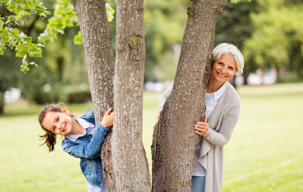 grandmother and granddaughter behind tree at park - Foto, afbeelding