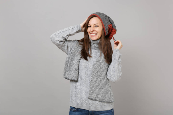 Pretty young woman in gray sweater hat and scarf putting hands on head isolated on grey background in studio. Healthy fashion lifestyle people sincere emotions cold season concept. Mock up copy space - Photo, Image