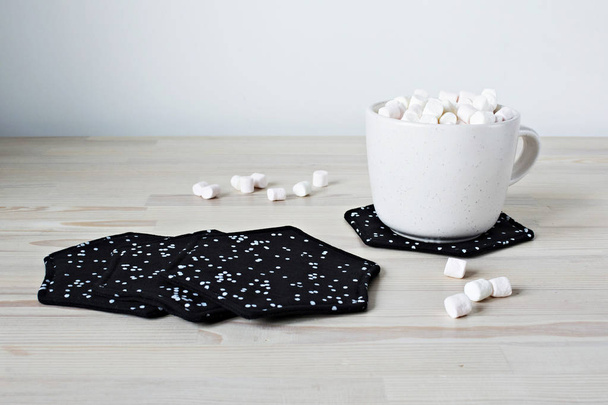  Black fabric coasters and white cup with marshmallows on the table - Foto, imagen
