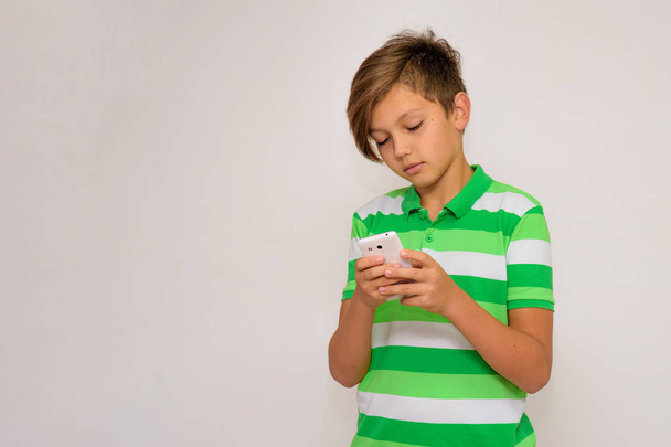 Studio portrait of a teenager boy on a white background with a smartphone. He stands directly in front of the camera and touches the phone. - Fotoğraf, Görsel