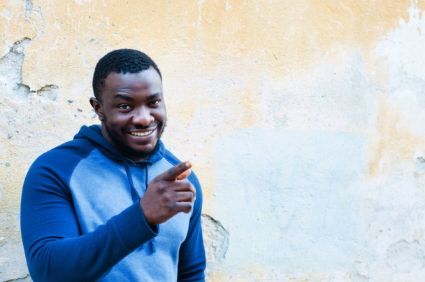 Portret van een close-up van de vrolijke positieve zwarte jongen in een trui sporten tegen een lichte muur achtergrond. Race kwesties. De foto van de stad, ruimte. Jeugdige cultuur. - Foto, afbeelding