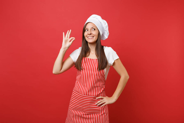 Hausfrau Köchin Köchin oder Bäcker in gestreifter Schürze weißes T-Shirt, Haubenköche Hut isoliert auf rotem Wandhintergrund. lächelnd ruhige süße Frau macht okay Geschmack Freude Zeichen. Attrappe Kopierraum-Konzept - Foto, Bild