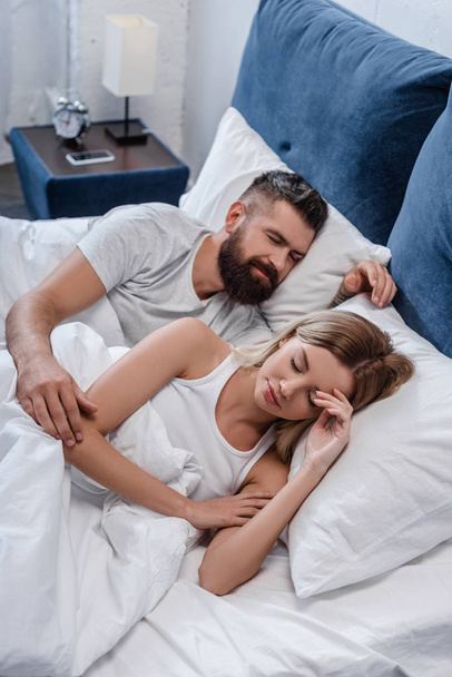 bärtiger junger Mann und schönes Mädchen schlafen morgens im großen weißen Bett - Foto, Bild