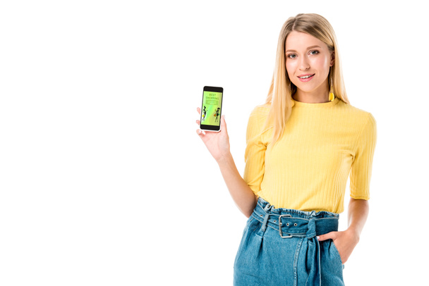 beautiful young woman holding smartphone with shopping application on screen and smiling at camera isolated on white  - Photo, Image