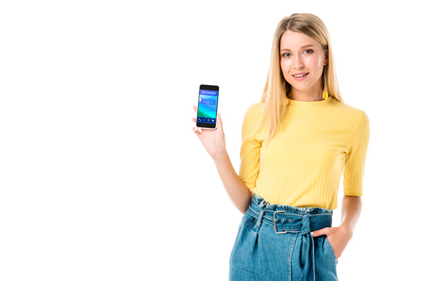 piękna młoda kobieta trzymając smartfon z aplikacją rezerwacji na ekranie i uśmiecha się do kamery na białym tle  - Zdjęcie, obraz