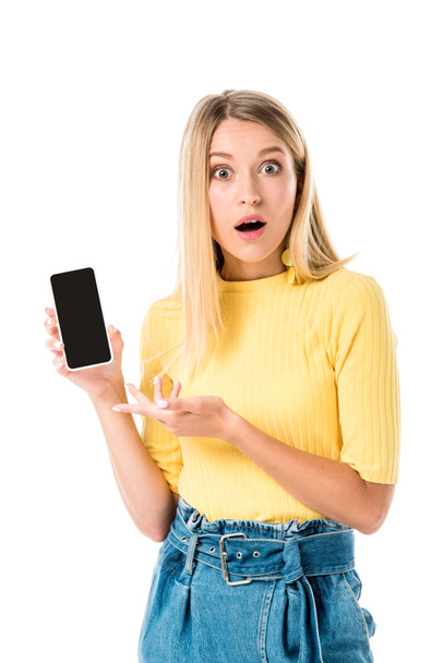 shocked young woman showing smartphone with blank screen and looking at camera isolated on white - Photo, Image