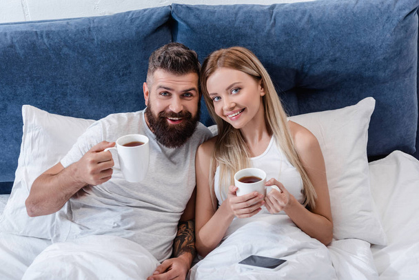 happy couple lying in bed and drinking coffee in morning - Foto, Imagem