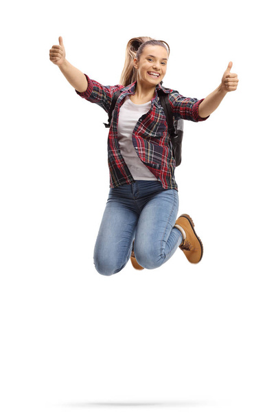 Full length shot of a female student jumping and showing thumbs up isolated on white background - Fotografie, Obrázek