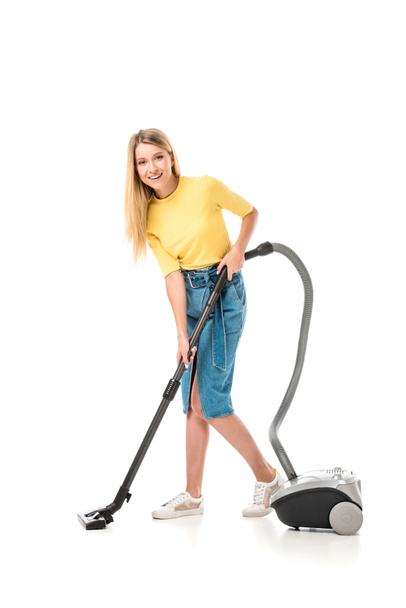 beautiful young woman using vacuum cleaner and smiling at camera isolated on white   - Фото, изображение