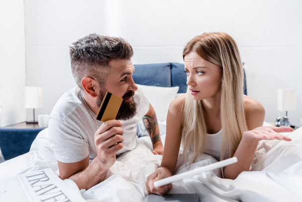 Jeune couple avec tablette numérique couché dans le lit et faire des achats en ligne
 - Photo, image