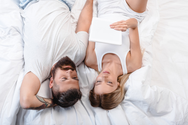 young couple lying in bed and looking at white digital tablet - Foto, imagen