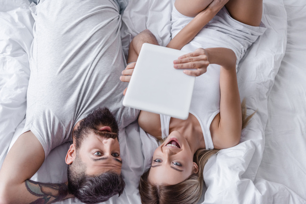 surprised couple lying in bed and looking at digital tablet - Fotó, kép
