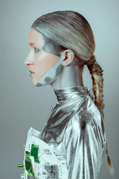 Seitenansicht des futuristischen silbernen Cyborgs, der isoliert auf grauem, zukünftigem Technologiekonzept wegschaut - Foto, Bild