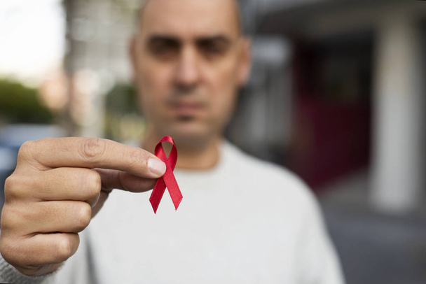 Close-up van een jonge man met een rode bewustzijn lint voor de strijd tegen Aids in zijn hand - Foto, afbeelding