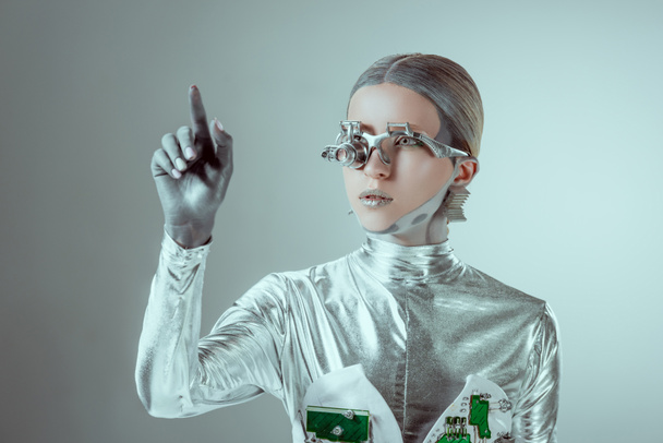 futuristic silver cyborg gesturing with hand and looking away isolated on grey, future technology concept   - 写真・画像