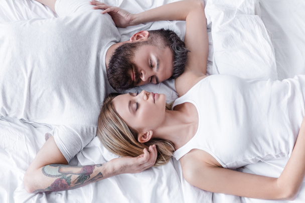 pretty couple in love lying head to head and sleeping in white bed - Foto, Bild