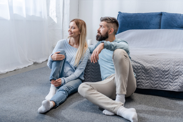 felice giovane coppia seduta sul pavimento e guardando la finestra in camera da letto blu
 - Foto, immagini
