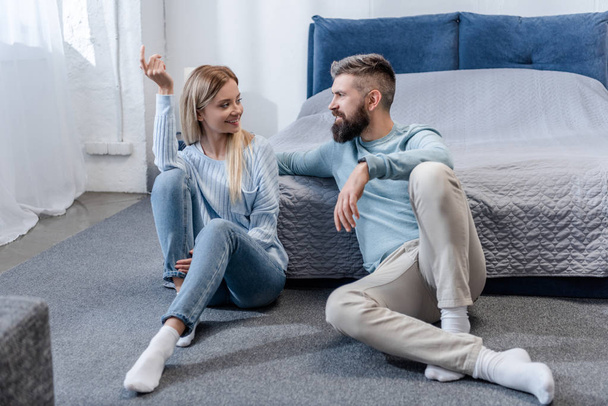 Nuori tyttö ja komea mies istuu lattialla ja puhuu sinisessä makuuhuoneessa
 - Valokuva, kuva