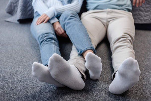 Ausgeschnittene Ansicht eines Paares, das mit überkreuzten Beinen auf dem Boden sitzt - Foto, Bild