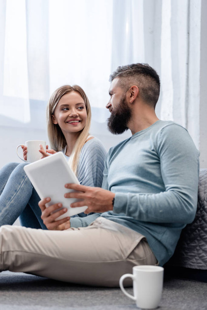 Couple souriant et assis dans des vêtements décontractés avec tablette numérique
  - Photo, image