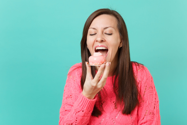 Mujer joven bonita en suéter de punto rosa mantener los ojos cerrados, agarrar la mano y comer pastel aislado sobre fondo de pared azul turquesa, retrato de estudio. Concepto de estilo de vida. Simular espacio de copia
 - Foto, Imagen
