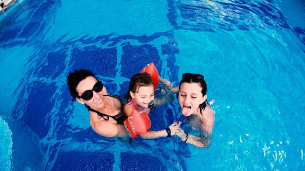 Aerial view of family mother and daughters having fun in luxury pool. Thay stick Tongue Out, Make Funny Faces smiling, slow motion - Фото, изображение