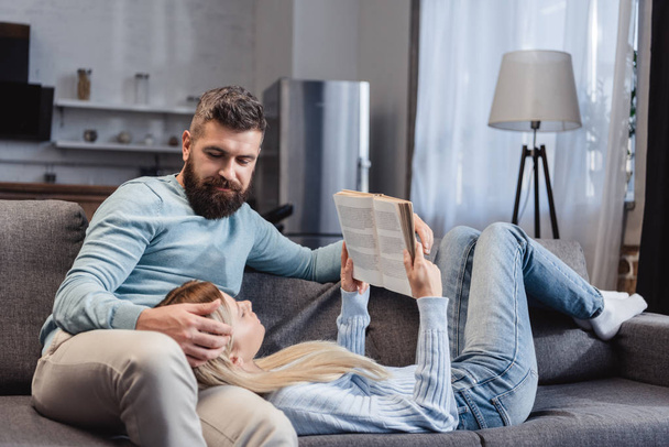  Wife reading book and lying on knees of handsome husband - Foto, Imagen