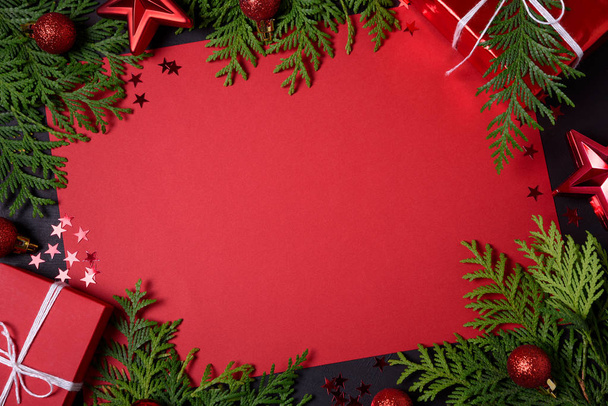 Christmas frame of red gift boxes, fir branches, confetti, paper for text and toys on black background. Flat lay. Top view. Copy space - Photo, Image
