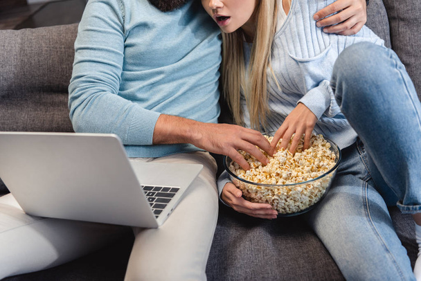 Croped view of couple sitting on sofa and watching movie on laptop  - Photo, Image